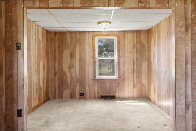 carpeted spare room featuring wooden walls and a paneled ceiling