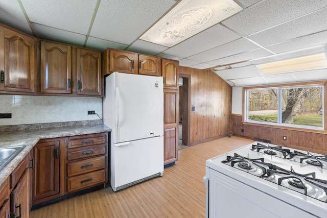 kitchen with wooden walls, white appliances, light wood-style flooring, a drop ceiling, and tasteful backsplash