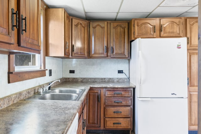 kitchen featuring brown cabinetry, backsplash, a sink, light countertops, and white appliances