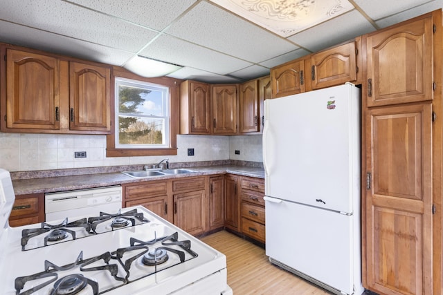kitchen with a sink, a drop ceiling, brown cabinets, and white appliances