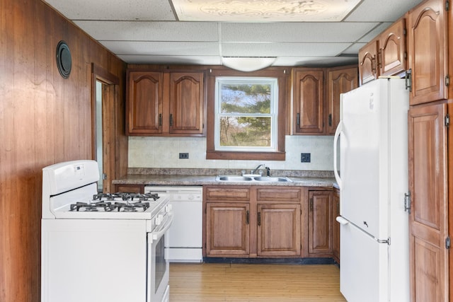 kitchen with white appliances, brown cabinets, a drop ceiling, and a sink