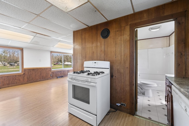 kitchen with white gas range, visible vents, a wainscoted wall, light wood finished floors, and wooden walls