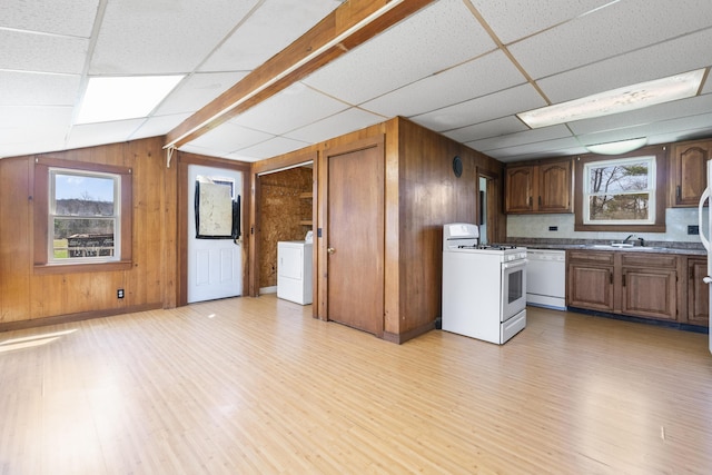 kitchen featuring washer / dryer, light wood finished floors, white appliances, and wooden walls