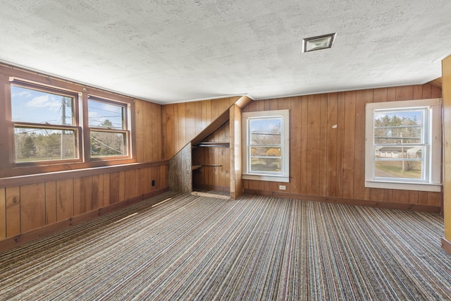unfurnished living room with carpet floors, wooden walls, a textured ceiling, and baseboards