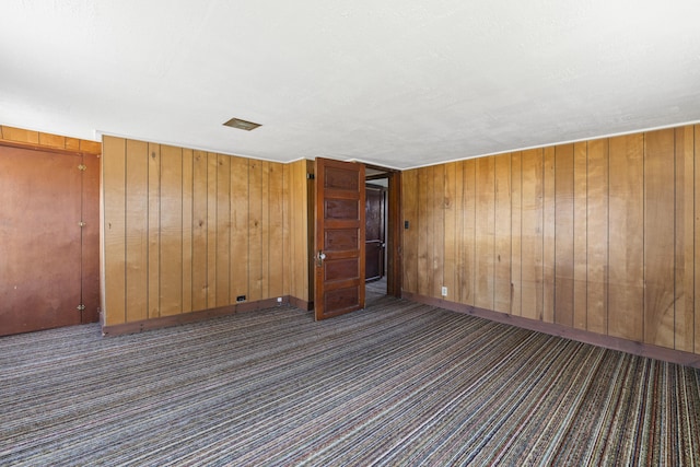 carpeted empty room featuring wooden walls