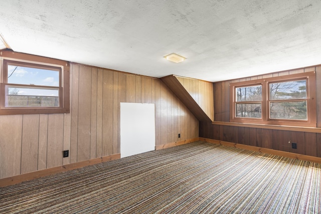 bonus room with carpet flooring, wood walls, and a textured ceiling
