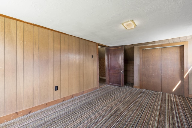 unfurnished bedroom featuring a textured ceiling, wood walls, carpet, and a closet