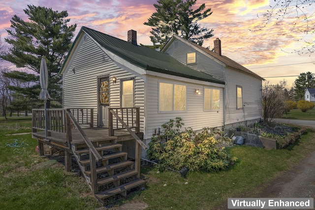 back of house at dusk featuring a wooden deck, a yard, and a chimney