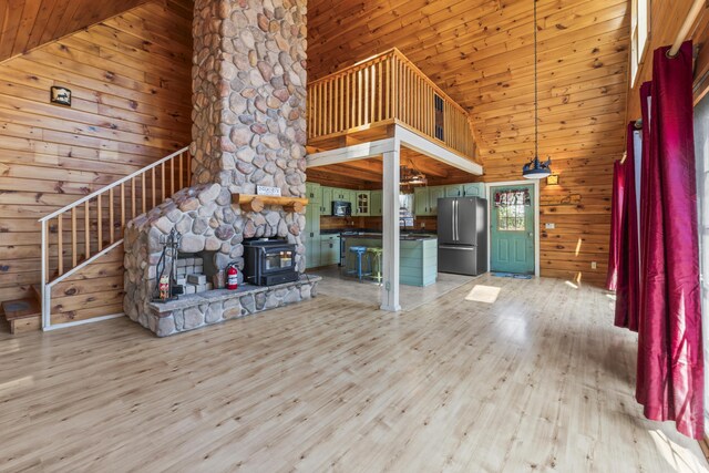 48 Thistle Ln, Sidney, ME 04330 - unfurnished living room with light wood-style floors, wood walls, high vaulted ceiling, a wood stove, and stairs