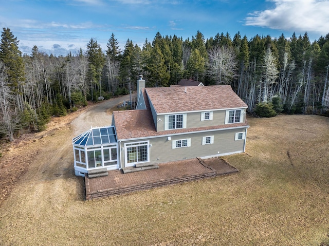 back of property featuring a lawn, a chimney, and a view of trees