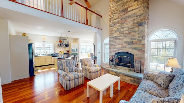 living room with a towering ceiling, a stone fireplace, and wood finished floors
