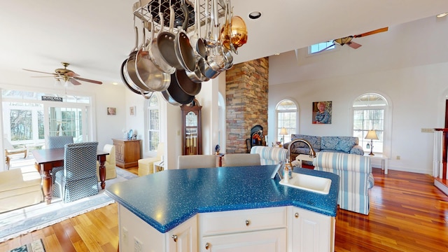 kitchen with wood finished floors, ceiling fan, a sink, white cabinetry, and open floor plan