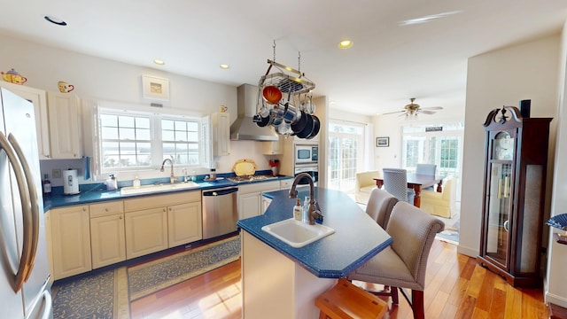 kitchen featuring a breakfast bar area, stainless steel appliances, light wood-style floors, a sink, and wall chimney exhaust hood