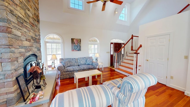 living area with wood finished floors, a ceiling fan, high vaulted ceiling, and a stone fireplace
