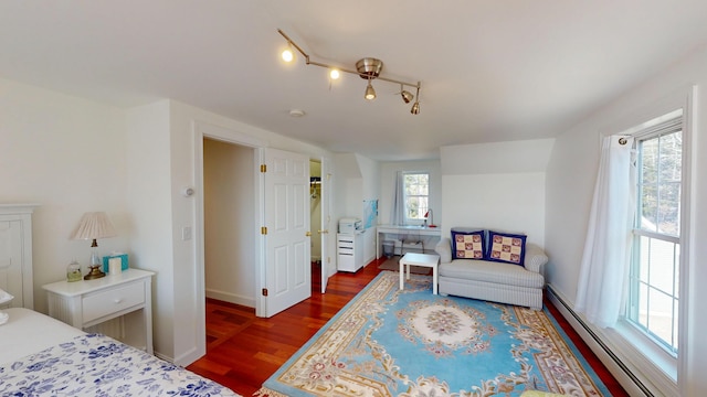 bedroom with dark wood-style floors, a baseboard heating unit, and baseboards
