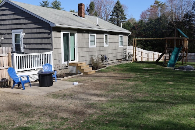 rear view of property featuring a lawn, a playground, fence, and a chimney