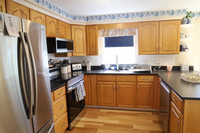 kitchen featuring light wood finished floors, backsplash, dark countertops, and stainless steel appliances