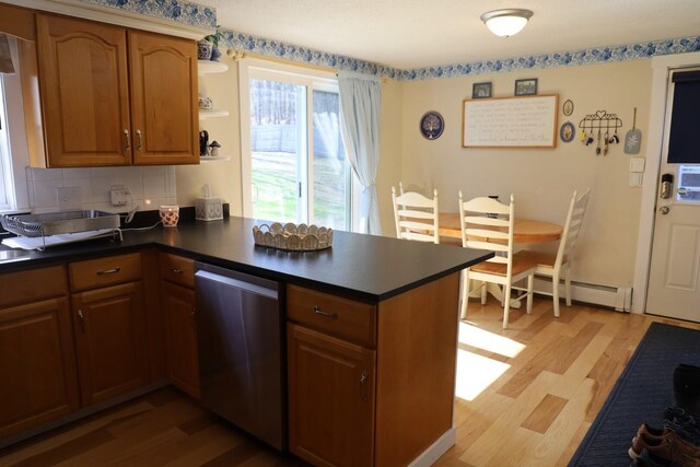 kitchen featuring a peninsula, dark countertops, light wood-style floors, a baseboard heating unit, and dishwasher