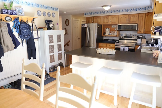 kitchen featuring dark countertops, appliances with stainless steel finishes, light wood-type flooring, a sink, and a peninsula
