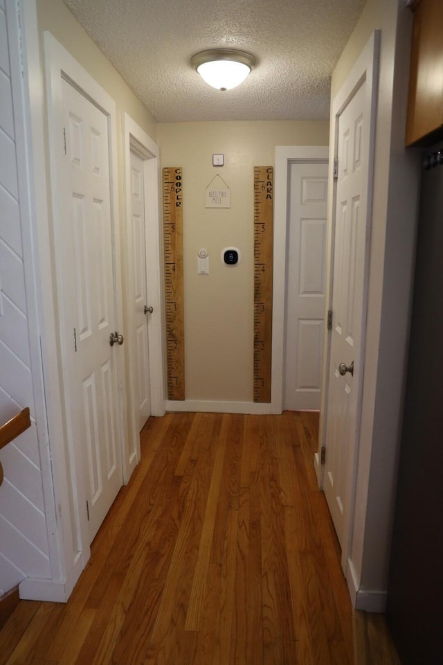 corridor with baseboards, a textured ceiling, and wood finished floors