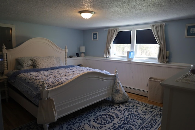 bedroom featuring wood finished floors, a textured ceiling, a baseboard heating unit, and a wainscoted wall