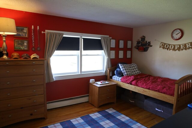 bedroom with a textured ceiling, wood finished floors, and a baseboard radiator