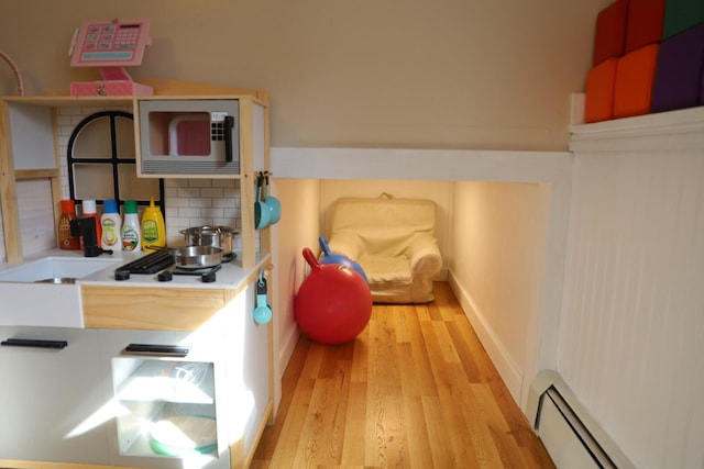 interior space with baseboard heating, light wood-style floors, light countertops, built in microwave, and tasteful backsplash