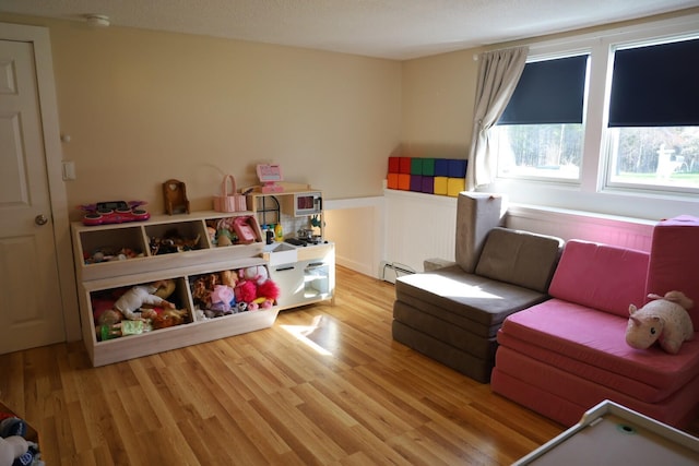 playroom featuring a baseboard radiator, light wood-style flooring, and a wainscoted wall