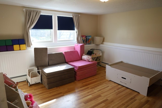 living area featuring wainscoting, a baseboard heating unit, and wood finished floors