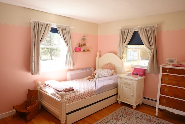 bedroom featuring a baseboard radiator, wood finished floors, and multiple windows