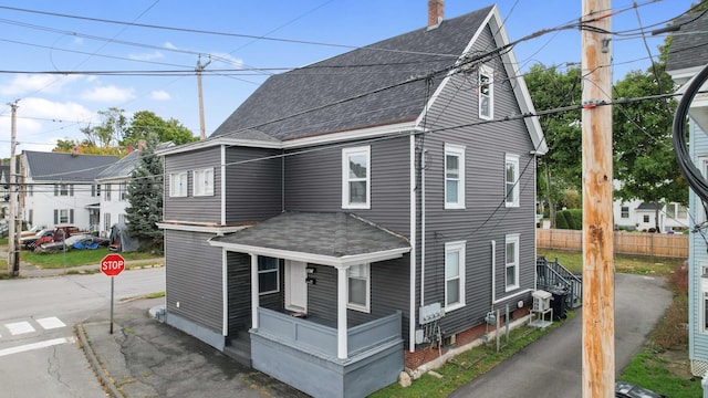 view of home's exterior with covered porch, fence, a chimney, and roof with shingles