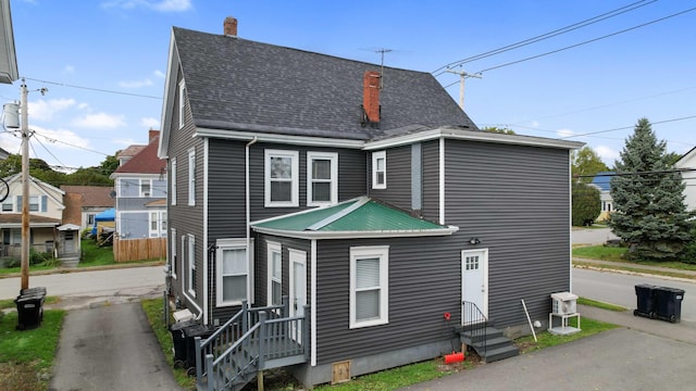 rear view of property with a shingled roof, entry steps, and a chimney