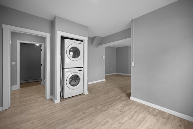 laundry room with baseboards, baseboard heating, stacked washer and clothes dryer, and light wood-type flooring