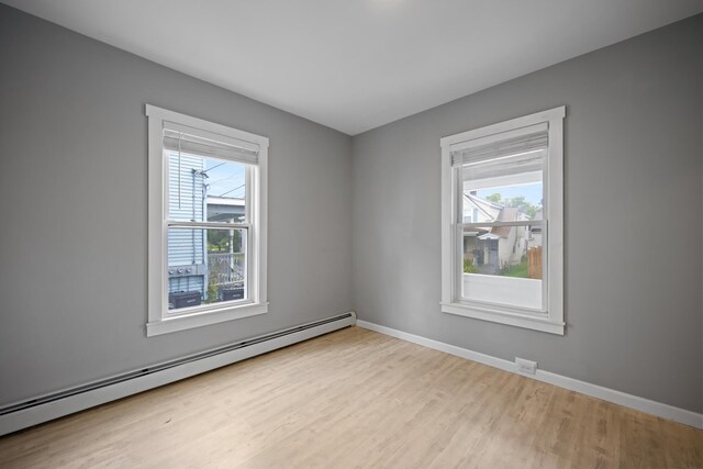 empty room featuring wood finished floors, a baseboard heating unit, and baseboards