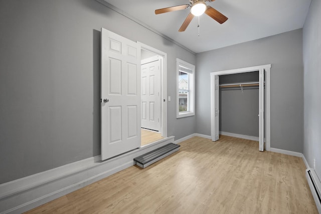 unfurnished bedroom featuring a baseboard heating unit, a closet, baseboards, and light wood-style floors