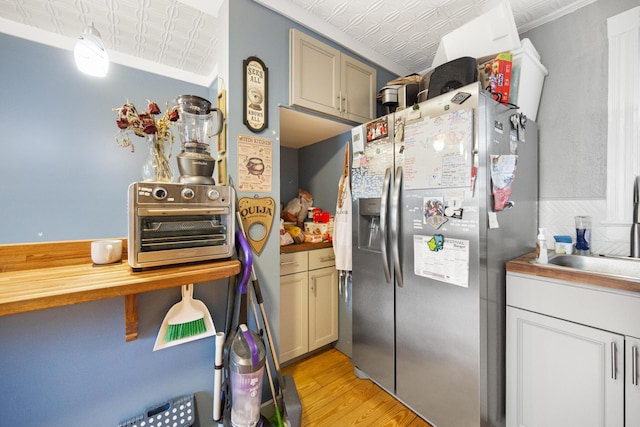 kitchen with stainless steel fridge, a sink, an ornate ceiling, and light wood-type flooring