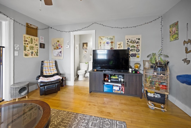 living area with wood-type flooring, a ceiling fan, and baseboards