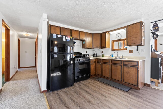 kitchen featuring black appliances, a sink, light wood-style flooring, and light countertops