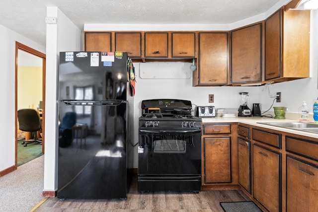 kitchen featuring black appliances, wood finished floors, light countertops, and brown cabinets