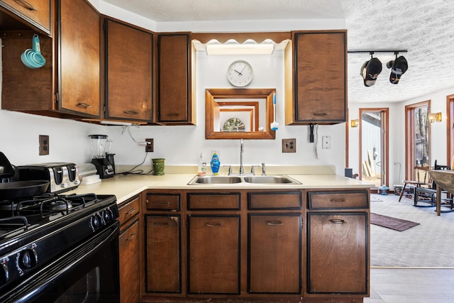 kitchen with black gas range oven, a textured ceiling, light countertops, and a sink