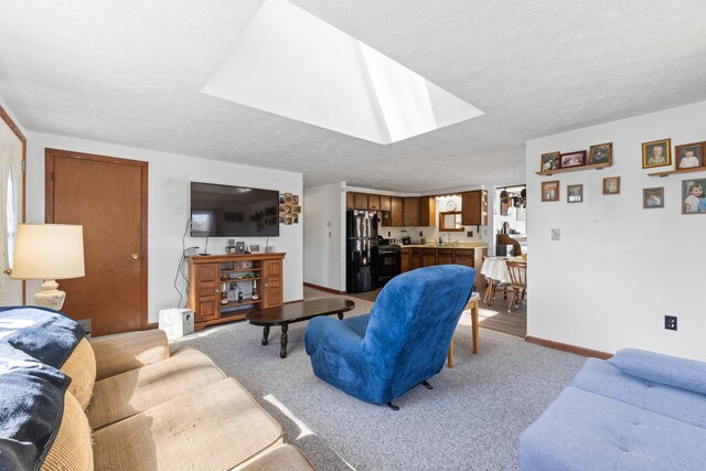 living area featuring baseboards, a skylight, a textured ceiling, and light colored carpet