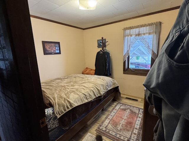 bedroom featuring visible vents, wood finished floors, and ornamental molding