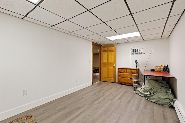 below grade area with a baseboard radiator, light wood-style floors, a paneled ceiling, and baseboards