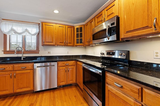 kitchen featuring brown cabinets, a sink, dark stone countertops, light wood-style flooring, and appliances with stainless steel finishes