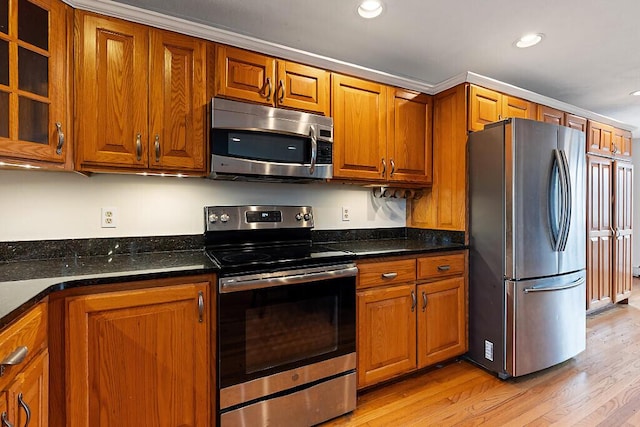kitchen with dark stone counters, appliances with stainless steel finishes, light wood finished floors, and brown cabinets