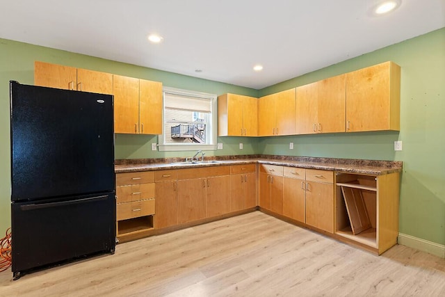 kitchen with dark countertops, a sink, light wood-style flooring, and freestanding refrigerator