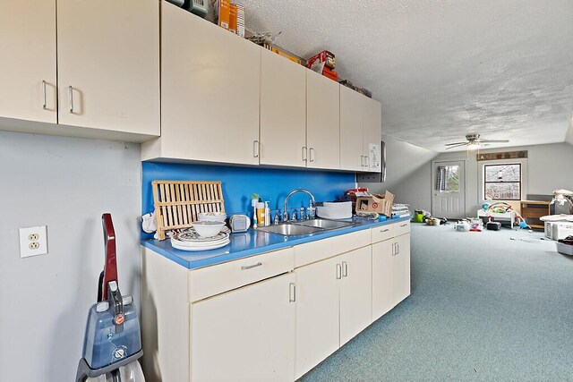 kitchen featuring a textured ceiling, white cabinets, a sink, open floor plan, and a ceiling fan