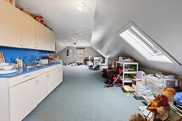 interior space with a ceiling fan, a sink, vaulted ceiling with skylight, and carpet floors