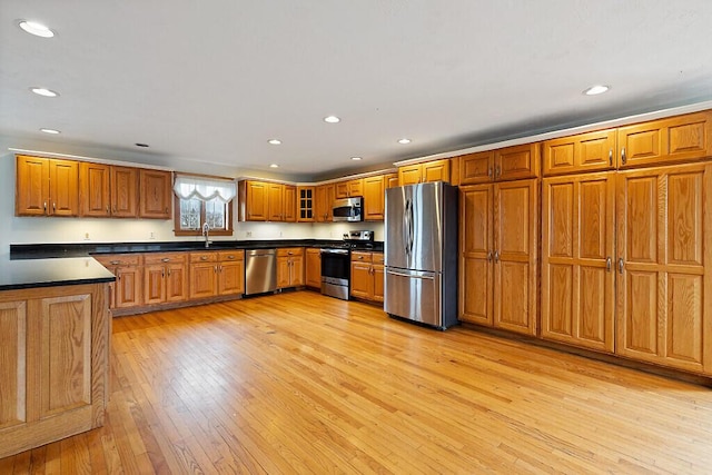 kitchen with recessed lighting, brown cabinets, stainless steel appliances, light wood-style floors, and dark countertops