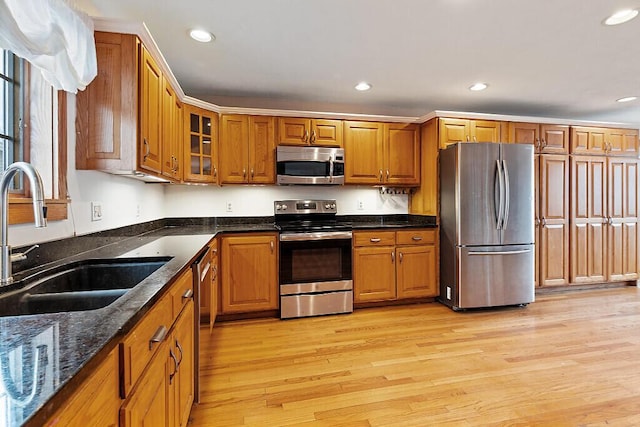 kitchen with stainless steel appliances, brown cabinets, light wood finished floors, and a sink